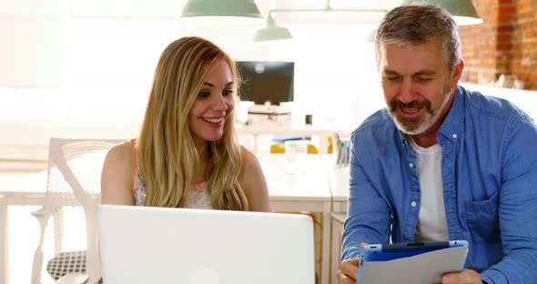 Male and female executives discussing over digital tablet at desk