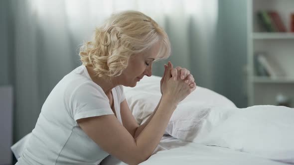 Caring Mother Sitting Near Bed and Praying for Children, Hope and Religion