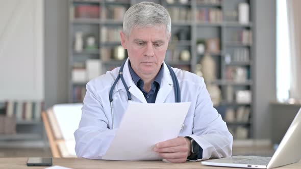 Professional Middle Aged Doctor Reading Documents While Sitting in Office