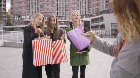 Three Happy Girls with Shopping Bags Posing for Their Fourth Friend Taking Photoes. Four Fashion