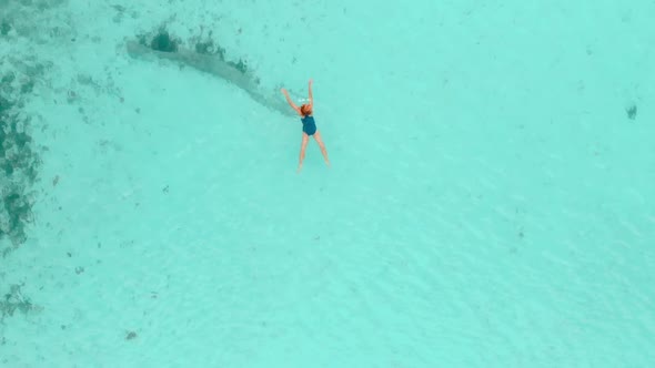 Aerial slow motion: top down woman swimming on turquoise transparent water
