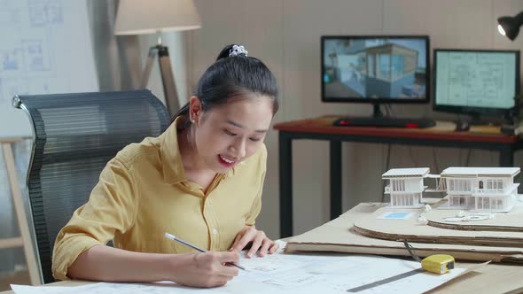 Asian Woman Engineer With A Laptop Looking At Blueprint While Working At The Office