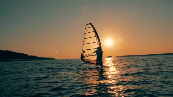 Sailboarder Is Crossing the Ocean at Sunset