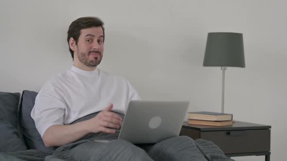 Young Man with Laptop Showing Thumbs Up in Bed