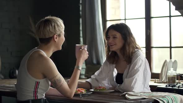 Young Lesbian Couple is Eating and Talking While Sitting at Table in Apartment