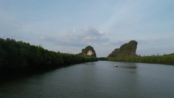 Aerial drone flying low along a river and mangrove forest approaching a thai longtail boat and limes