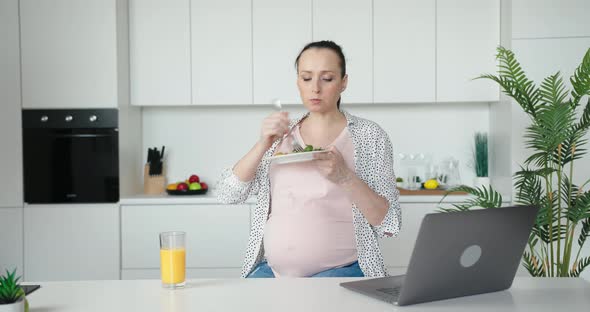 Gravid Woman Eats Fresh Salad and Drinks Juice in Kitchen