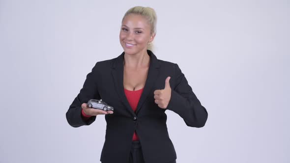 Young Happy Blonde Businesswoman Holding Toy Car and Giving Thumbs Up