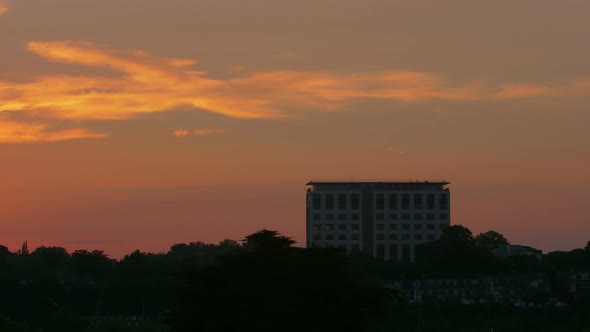 Wide dawn sunrise timelapse of a tall office building and trees silhouetted into the foreground.