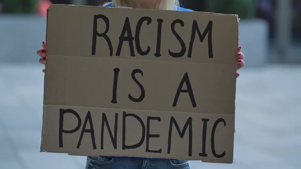 RACISM IS A PANDEMIC on a Cardboard Poster in the Hands of White Female Protester Activist. Closeup