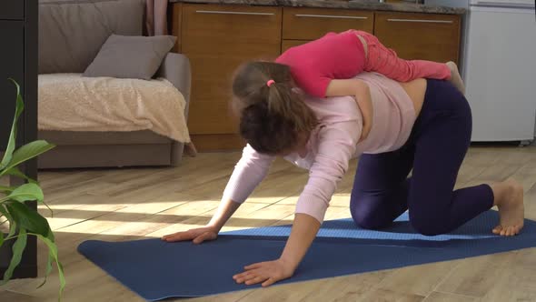 woman tries to do sports fitness yoga at home in the kitchen with her baby daughter. Lockdown