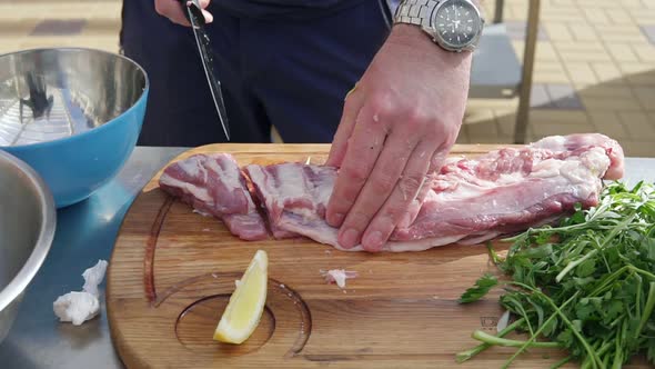 Person's Hands Cutting a Piece of Raw Meat Using a Butcher's Knife on a Wooden Surface Outside