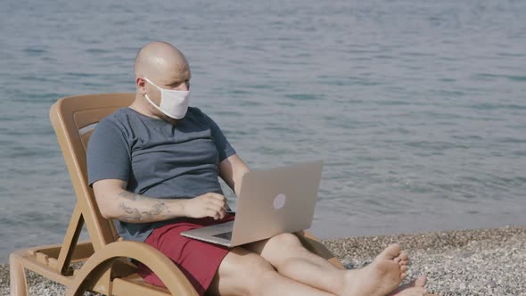 Man Freelancer in Medical Mask Work on Laptop By the Sea
