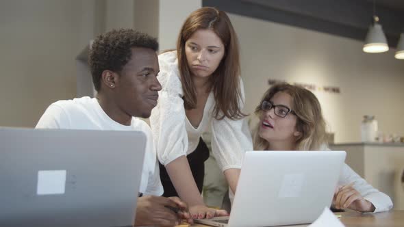 Creative Team Sitting and Standing at Table with Laptops