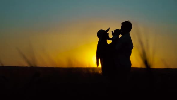 Silhouettes of Family with Baby Standing in Field at Sunset