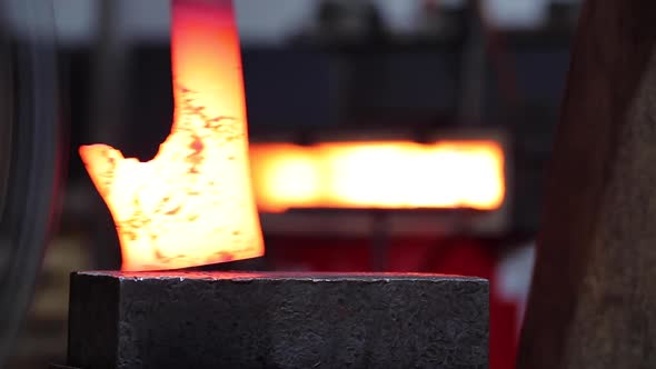 Blacksmiths forging hot metal with hammer in workshop