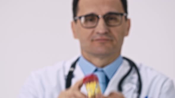 Middle Aged Doctor Shows Pack of Different Colored Pills on White Background