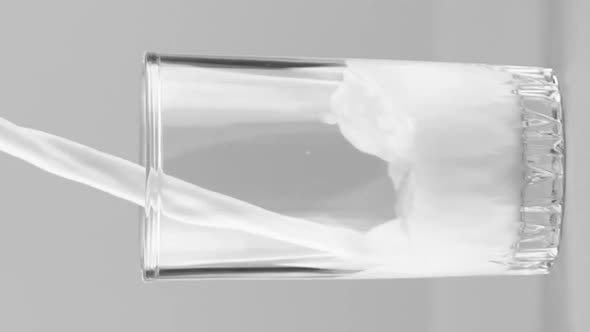 Vertical Video Milk Pouring Into Glass Close Up Isolated on Light Grey Background Slow Motion