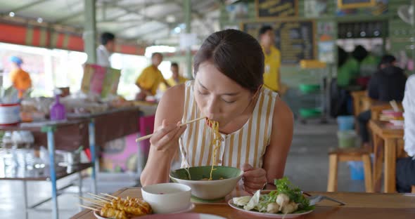 Woman eat with thai cuisine boat noodle at outdoor vendor store