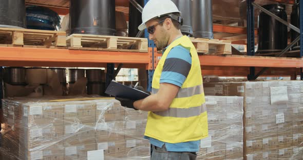 Logistics worker wearing a helmet working in a large warehouse checking inventory