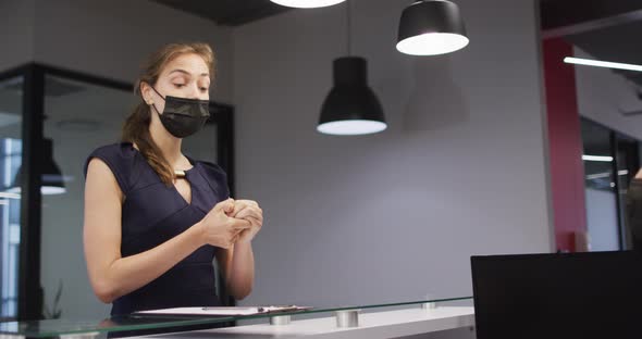 Caucasian woman in face mask disinfects hands and signs in at office reception desk