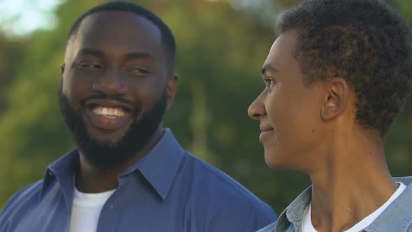 African-American Male and Teenage Boy Standing Shoulder to Shoulder and Smiling