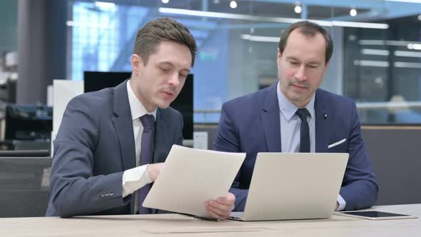 Two Businessman Working on Laptop with Documents in Office