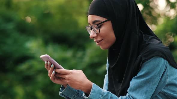 A side view of a happy arabian woman wearing black national hijab is using her mobile