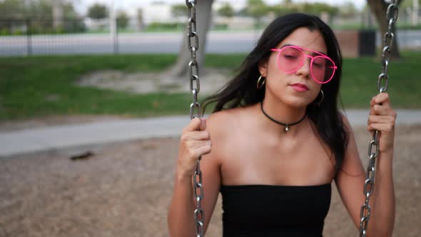 A beautiful young hispanic woman playing and swinging on a park playground swing set wearing retro p