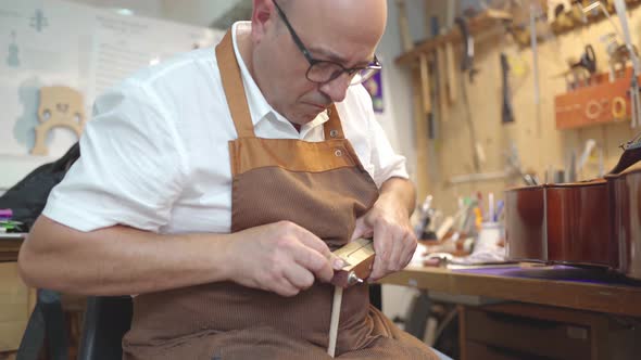 Luthier with violin bridge in workshop