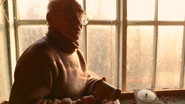 Elderly Man Glasses Picks Up Old Stuffs Brushing Dust Off in Attic House Window