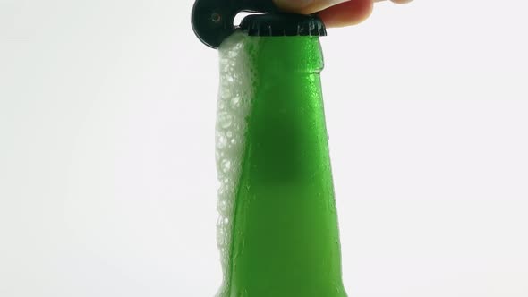 A Man Opens A Bottle Of Beer With An Opener, Frothy Beer Is Pouring From The Bottle