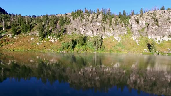 The mountains are reflected in the water of this mountain lake as steam raises