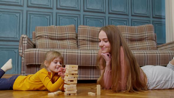 Happy Young Mother Woman Teaching Small Child Daughter Playing Wooden Blocks Board Game at Home