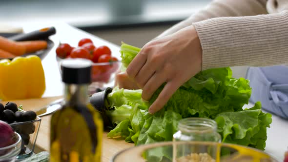 Woman Adding Lettuce To Salad Bowl at Home Kitchen