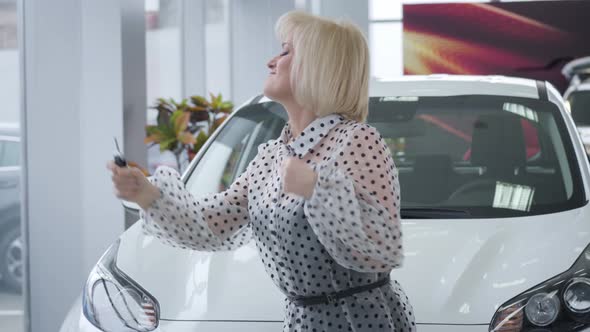 Cheerful Mature Caucasian Woman Dancing with Car Keys in Front of New Vehicle