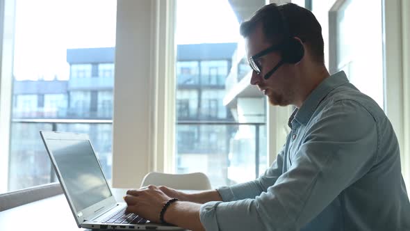 Confident Male Worker Sitting at the Desk with a Laptop and Working Remotely