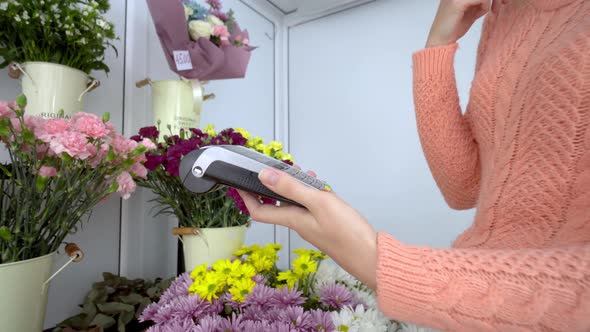female salesperson applies credit card to terminal against background of flowers