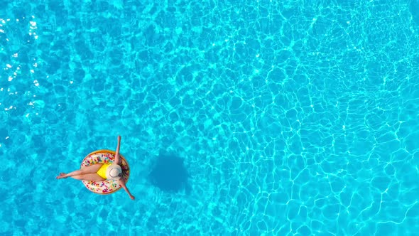 Aerial View of a Woman in Yellow Swimsuit Lying on a Donut in the Pool