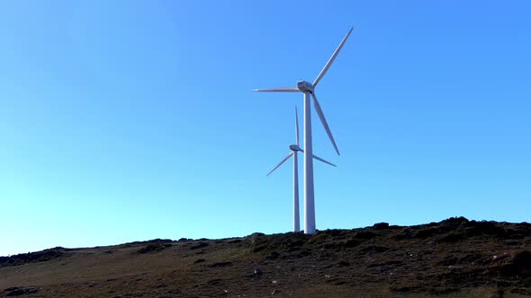 Two wind turbines with their blades spinning at the top of the mountain on a quiet, sunny afternoon