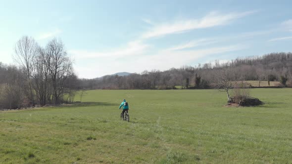 Aerial: man having fun by riding mountain bike in the grass on sunny day, scenic alpine landscape