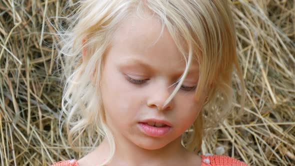 Girl Playing with a Straw on the Background of Haystacks