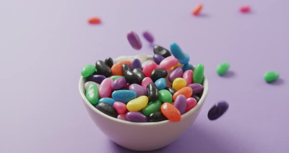 Video of close up of multi coloured sweets falling into bowl over purple background