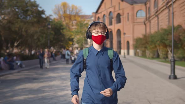 School Boy Wearing Face Mask Listening To Music in Headphones Walking Outdoors