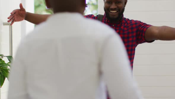 African american son running and hugging smiling father returning home at front door