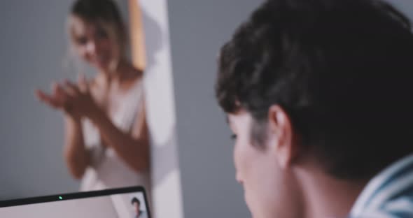 Young blonde woman whispering to man while he is in a video call