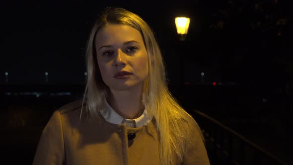 A Young Beautiful Woman Looks Seriously at the Camera in an Urban Area at Night