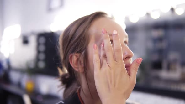 Makeup Artist Applies Foundation of a Beautiful Young Girl in the Makeup Studio Using Fingers and