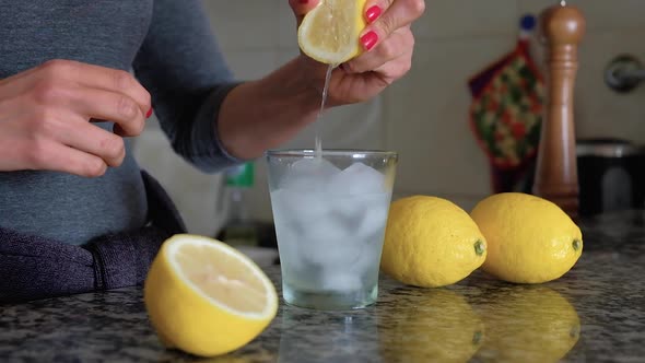 Slow Motion of woman squeezing lemon in glass with water and ice cubes