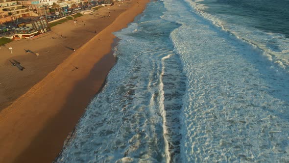 Aerial view above ocean waves tilting up to Reñaca beach Vina Del Mar coastal hotel resort buildings